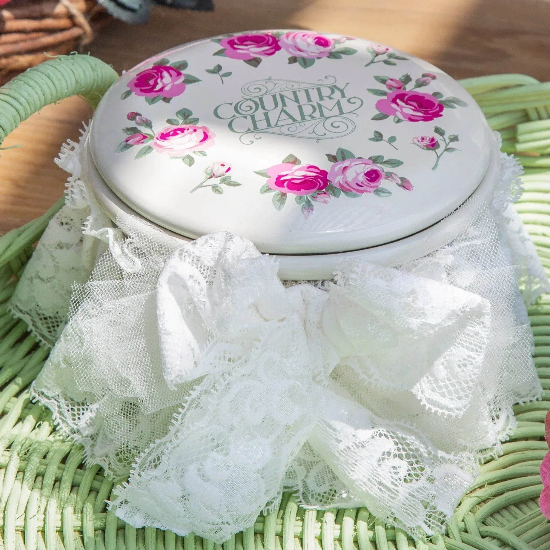 Vintage white tin container with pink floral design and 'Country Charm' text on green wicker basket, adorned with white lace
