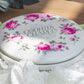 White tin container with pink floral design and 'Country Charm' text on wooden surface with lace fabric