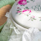 Close-up of white floral teapot lid with pink roses and lace fabric details in soft lighting