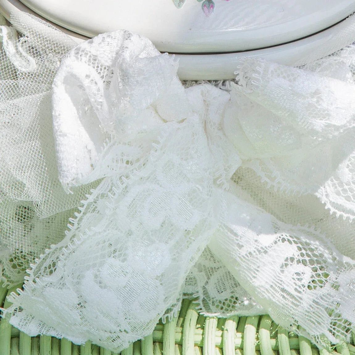 Close-up of white lace fabric with floral patterns on a woven surface and ceramic with floral design