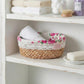 Floral-patterned basket with rolled towels on a white shelf.