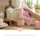 Hand holding a floral towel over a beige teapot on a kitchen counter with soft beauty theme.