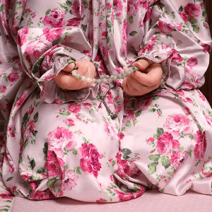 Person wearing a floral dress holding prayer beads.