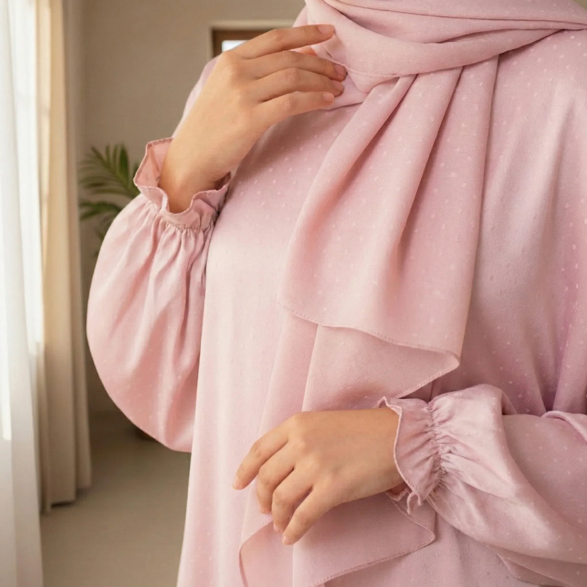 Person wearing a pink outfit with a matching hijab indoors.