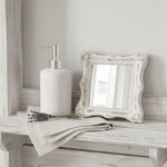 Ornate antique white square mirror on a distressed wood shelf with vintage keys and a small dried flower.