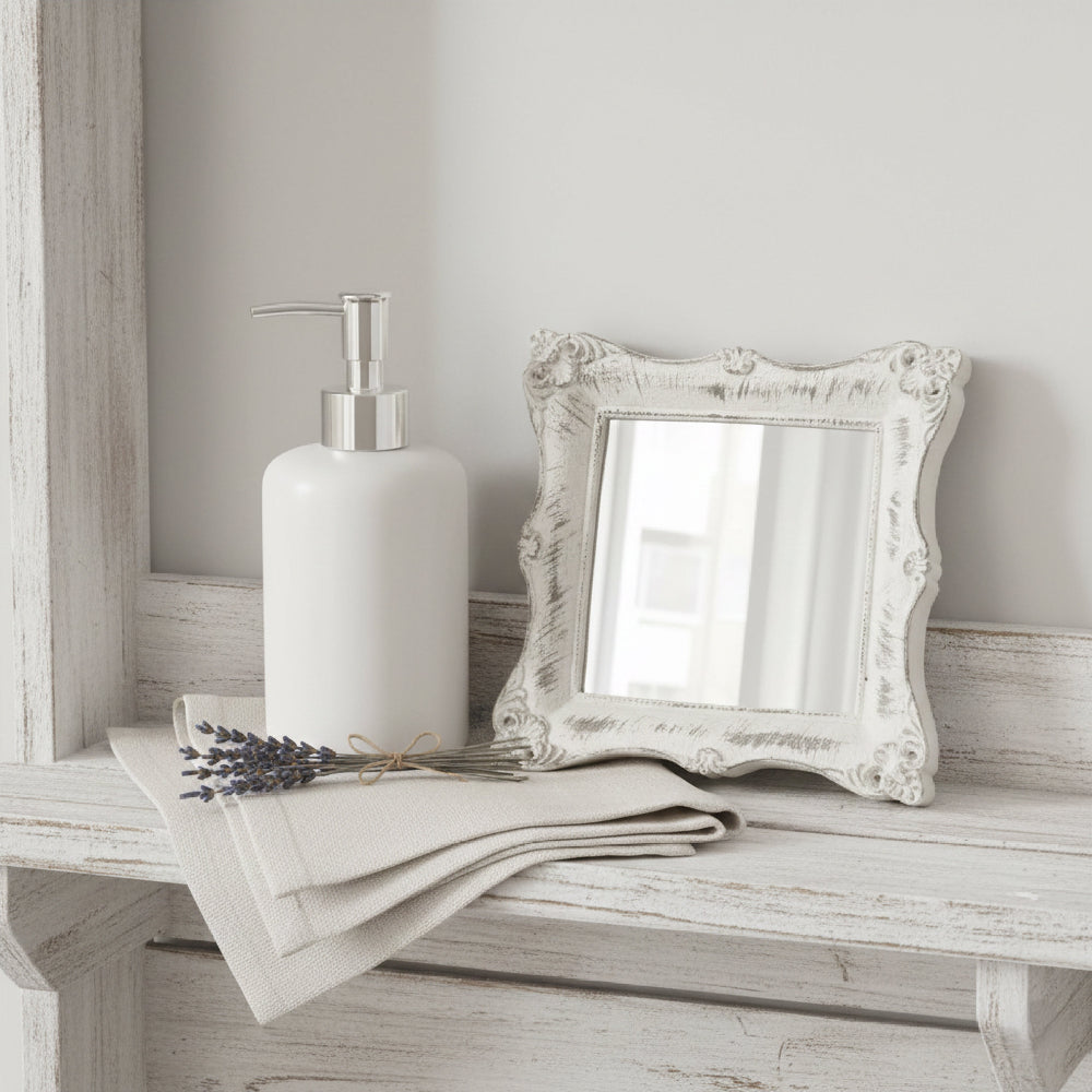 Ornate antique white square mirror on a distressed wood shelf with vintage keys and a small dried flower.