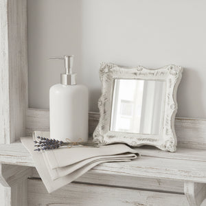 Ornate antique white square mirror on a distressed wood shelf with vintage keys and a small dried flower.