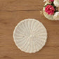 White round woven wicker placemat centered on a brown wood surface next to a vase with pink and cream flowers.