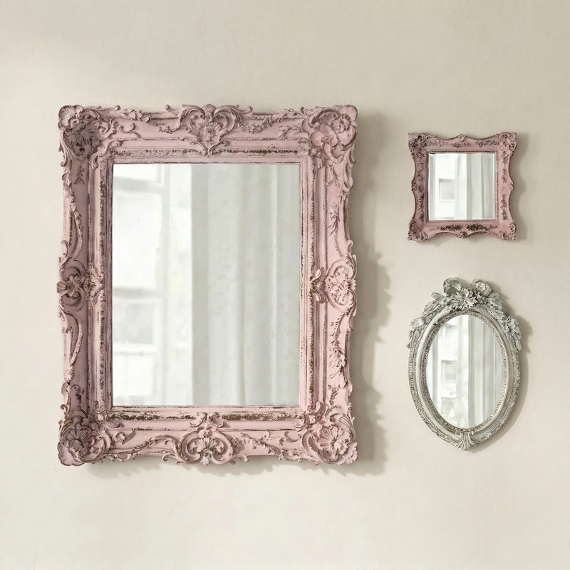 Three ornate mirrors with pink and gray frames on a light beige wall.