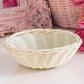 White wicker decorative bowl on table with pink flowers and ornate frame in background