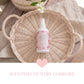 Bottle of 'air Kisses' on a woven basket with a heart and text overlay on a wooden surface.