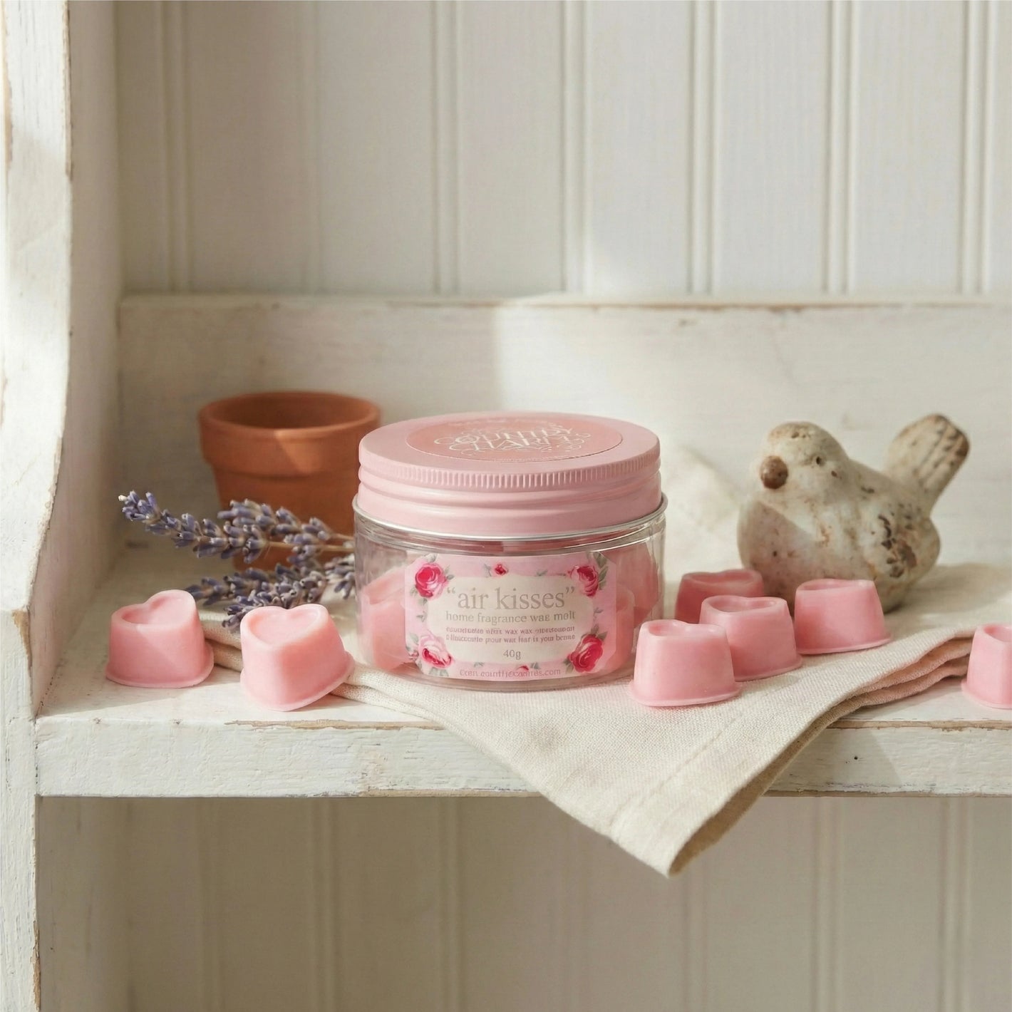 Jar of 'air kisses' with pink heart-shaped candles on a wooden shelf.

