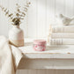 Air Kisses home fragrance soy wax melts jar on a distressed white wooden shelf with decorative books.