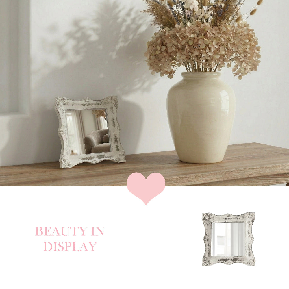 Antique white distressed mirror on a wood shelf next to a cream vase with dried flowers and a pink heart icon.