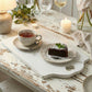 Antique white rectangular serving board with a heart-shaped handle, styled on a rustic wooden table with a steaming cup of tea, a slice of chocolate cake on a decorative plate, and lit candles.