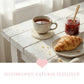 Cup of tea with a croissant and jar of jam on a wooden table, with 'Handwoven Natural Elegance' text.