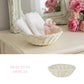 Antique white wicker basket on a vanity with lace towels and perfume, positioned next to pink flowers and a mirror.