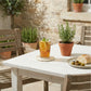 Antique white woven round coaster under a glass of iced tea on an outdoor rustic white table with rosemary plants and a bread plate.