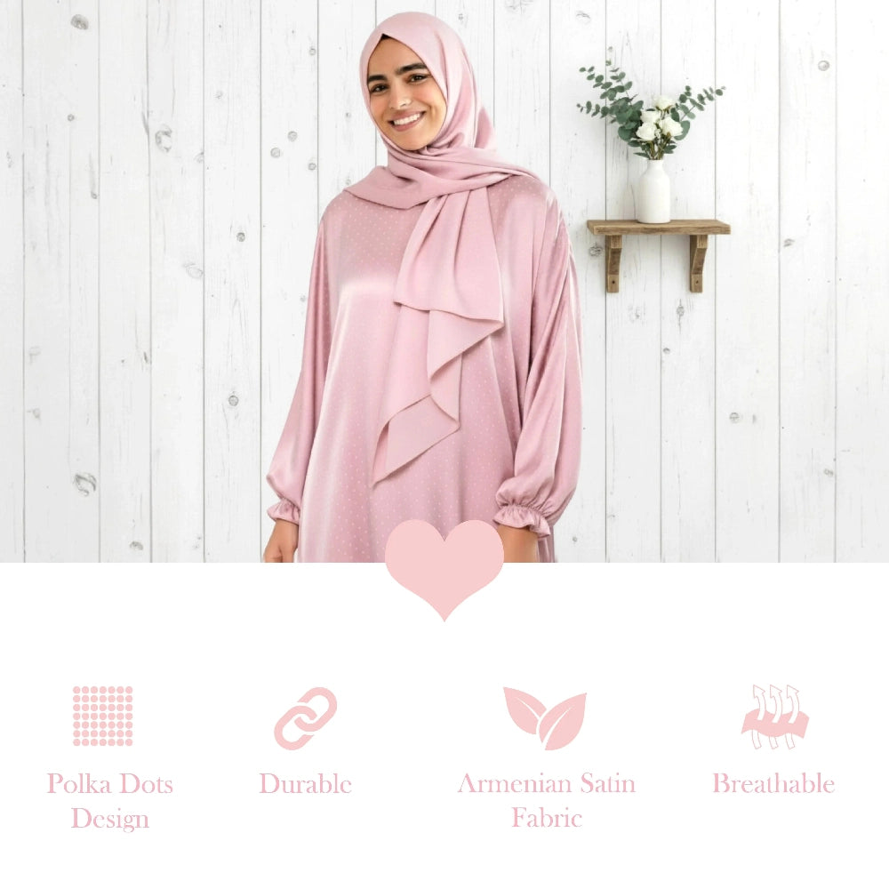 Woman wearing a pink hijab and polka dot Isdal Prayer dress against a white wooden background with text about fabric properties.