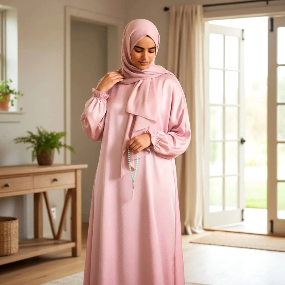Woman in a pink polka dot Isdal Prayer dress standing in a bright room with large windows.