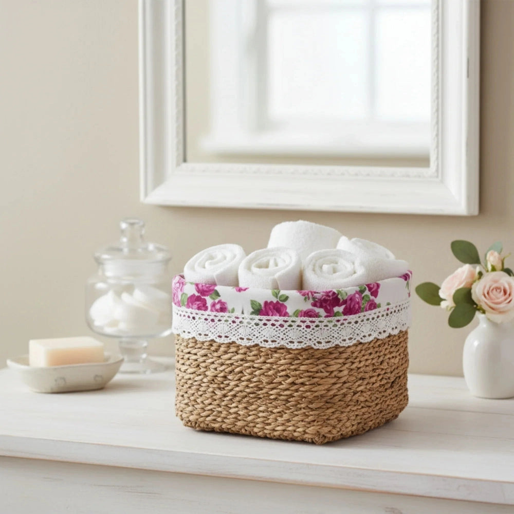 Basket with rolled towels and floral lace on a table with a vase and candle in the background