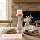Decorative setting with a candle, books, and a vase in front of a fireplace.