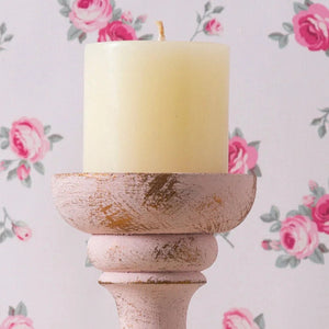 Candle in a rustic wooden holder against a floral wallpaper background