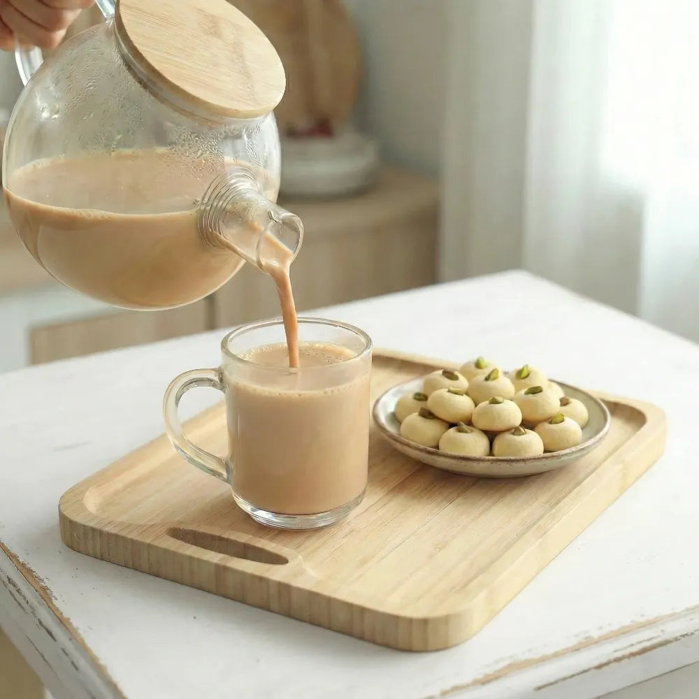 Glass carafe pouring coffee into a mug on a wooden tray with ghorayeba cookies.