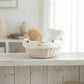 Cottage Round Wicker Basket with a hairbrush and white bowl on a wooden surface with a blurred background