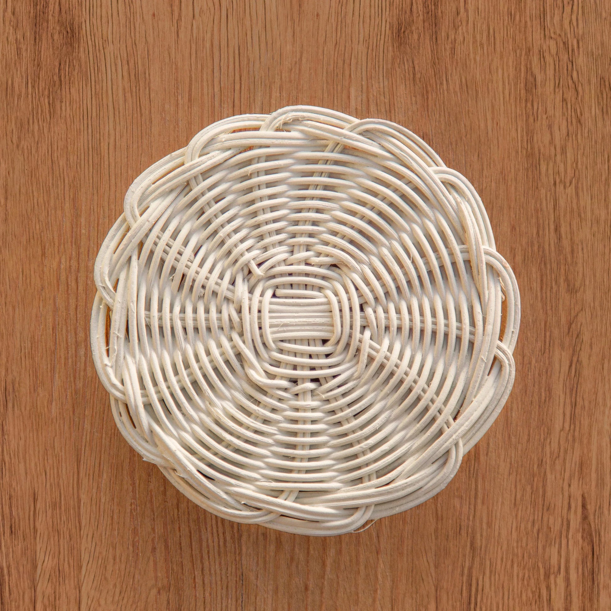 Round white wicker basket with intricate weave pattern on wooden surface