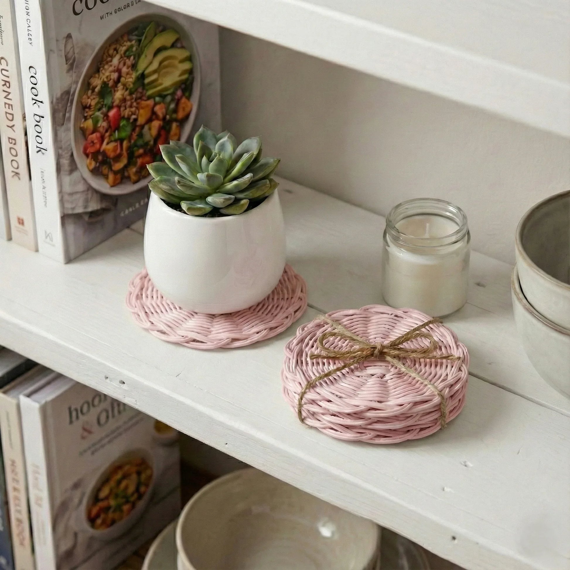 White shelf with a potted succulent, pink woven coasters, and a candle.