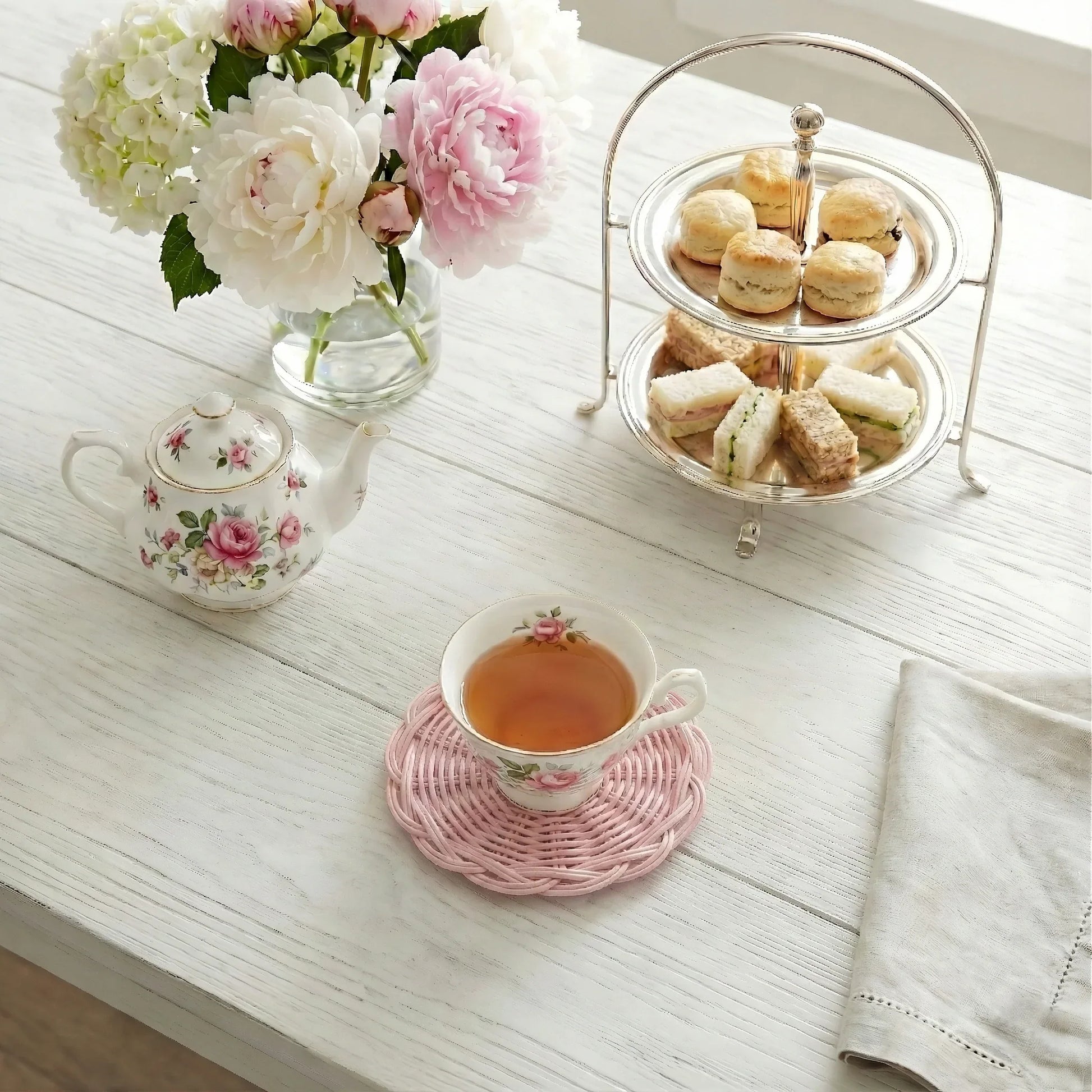 Tea set with teacup, teapot, and tray of pastries on a wooden table.