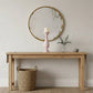 Wooden console table with a round mirror, candle, and basket in a room.