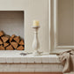 Candle in a decorative holder on a fireplace mantel with stacked logs and a framed picture.