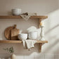 Wooden shelves with ceramic bowls, a cutting board, and a candle against a neutral wall.