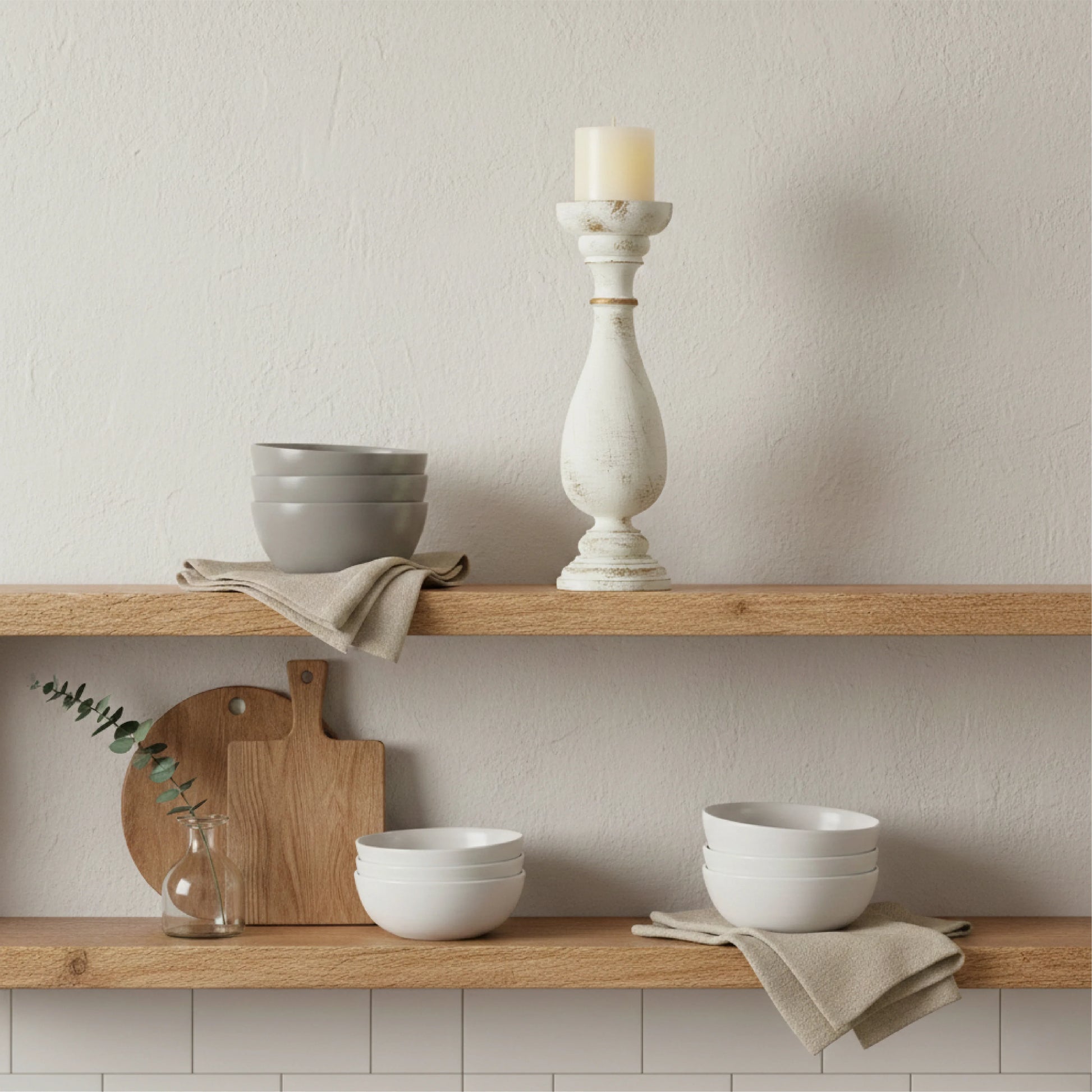 Wooden shelves with ceramic bowls, a candle holder, and a cutting board against a neutral wall.