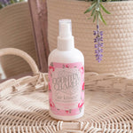 Bottle of Country Charm 'air kisses' room fragrance mist on a wicker surface with lavender in the background.