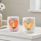 Two heart-shaped candle holders with candles inside on a white surface.

