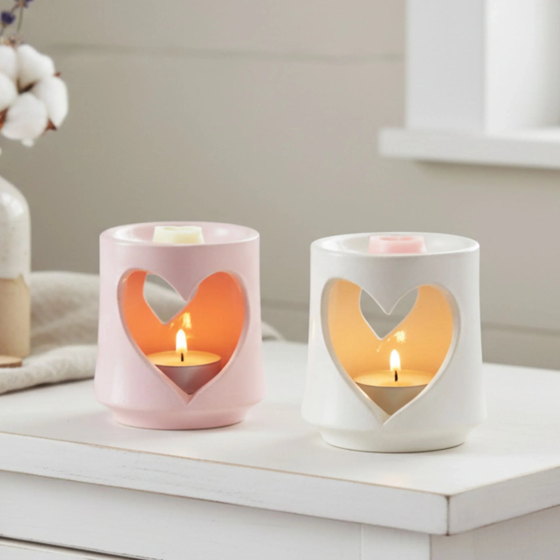 Two heart-shaped candle holders with candles inside on a white surface.

