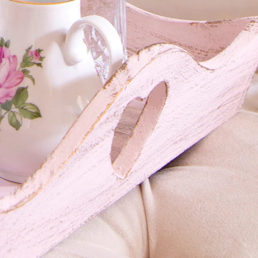 White wooden tray with heart-shaped handle holding floral teacup and glass on beige fabric