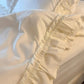 Close-up of a cream duvet cover with a wide ruffled edge resting on a white bed sheet.