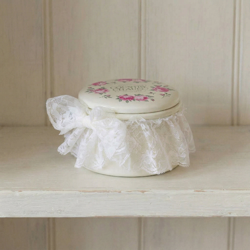 Decorative box with floral lid and lace ribbon on a wooden shelf.
