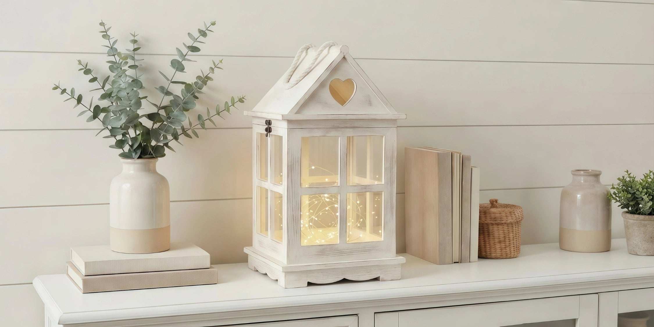 Decorative house-shaped lantern with books and plants on a white surface