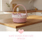 Pink wicker basket with floral interior on a wooden kitchen counter, with text 'Soft tones for cozy spaces'.