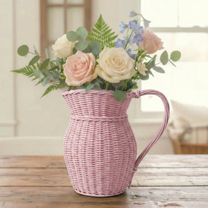 Pink wicker pitcher filled with flowers on a wooden surface
