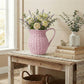 Pink woven pitcher with flowers on a wooden table in a home setting