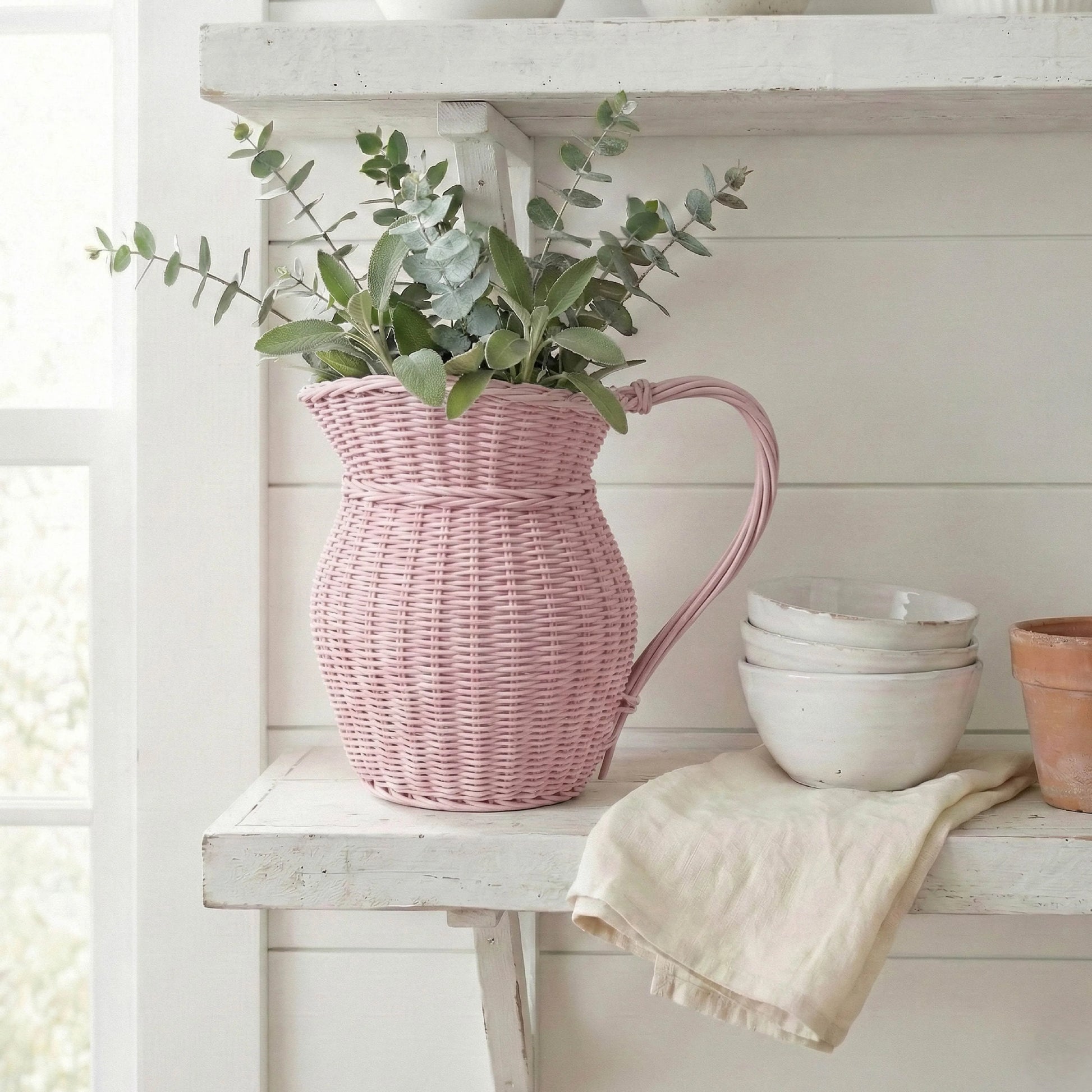 Pink wicker pitcher with greenery on a white wooden shelf