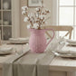 Pink woven vase with cotton branches on a dining table