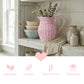Pink woven pitcher on a wooden shelf with decorative elements and text about material properties.
