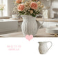 White wicker pitcher with pink flowers on a kitchen counter, with 'Beauty in Display' text and heart icon.